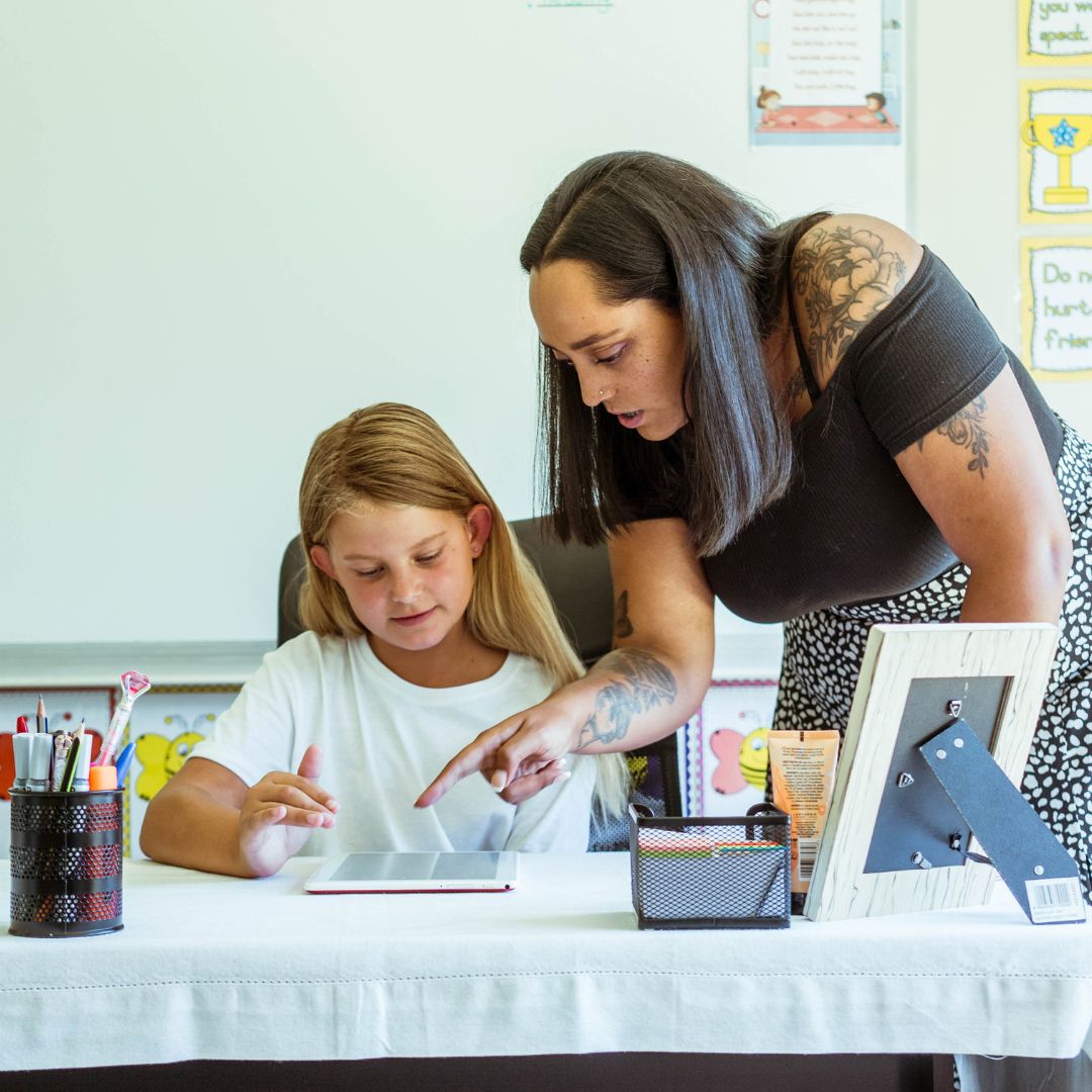 A teacher assists a child with learning grade 4 life orientation on a tablet using iRainbow.