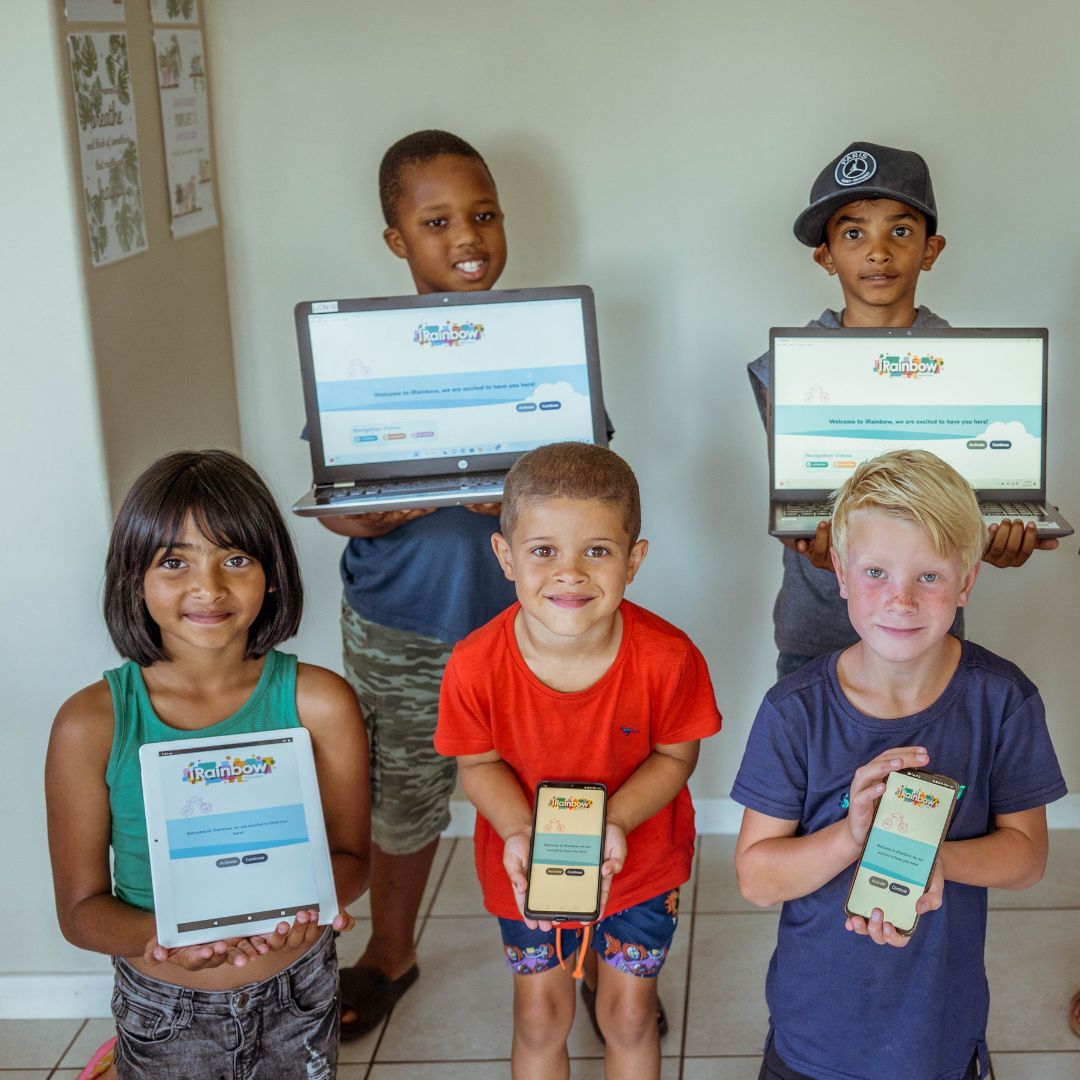 Children in a classroom are joyfully holding devices showcasing iRainbow's offline learning software.
