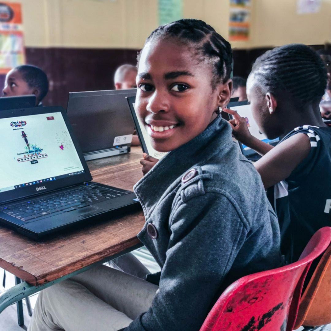 A happy student smiles in a classroom while exploring Grade 5 life orientation via iRainbow on her laptop.