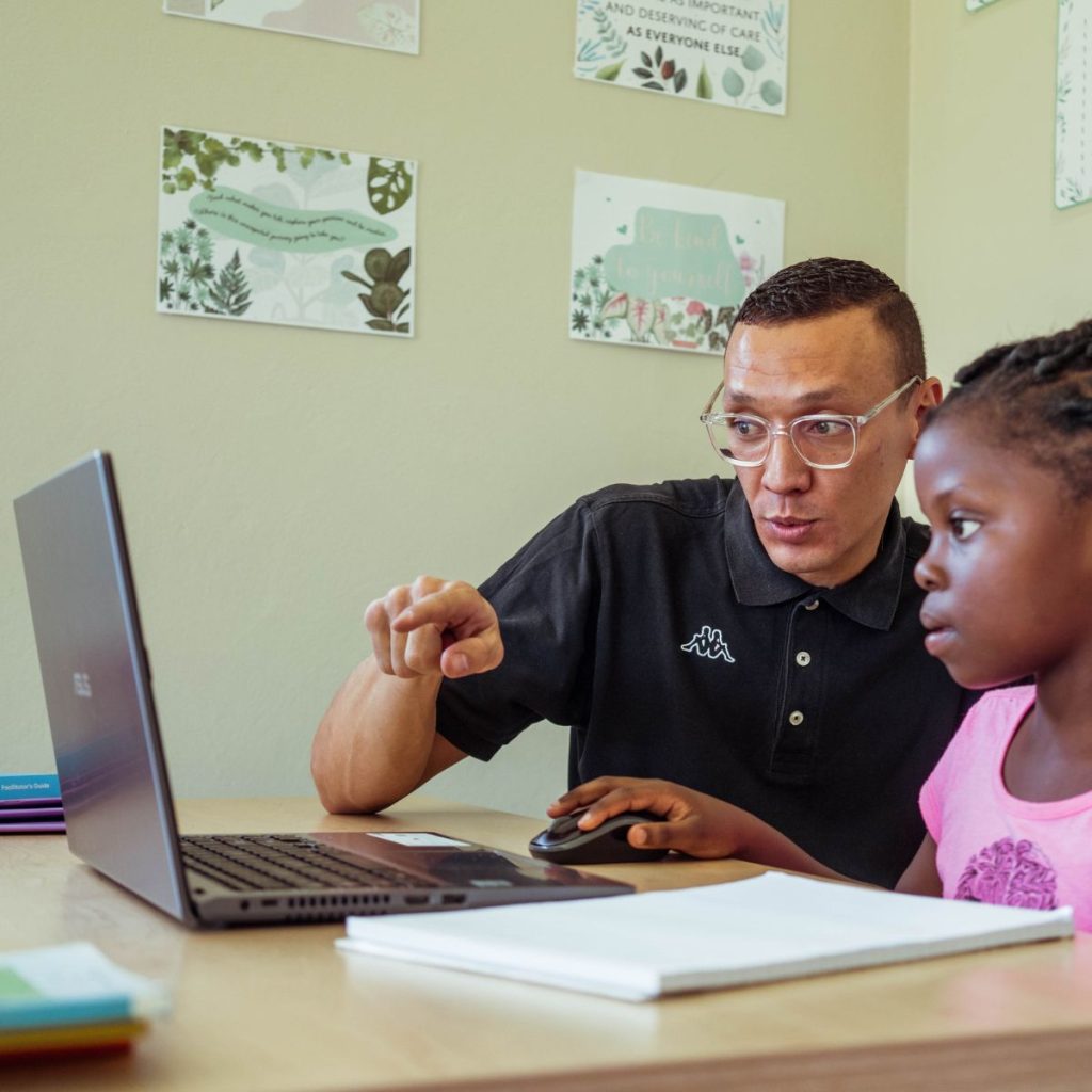 A child learning how to pass Afrikaans with a teacher and a laptop